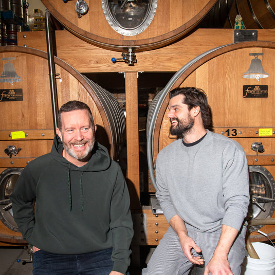 Co-founders Mike Clark and Luke Pestl sitting on kegs in front of oak foeders